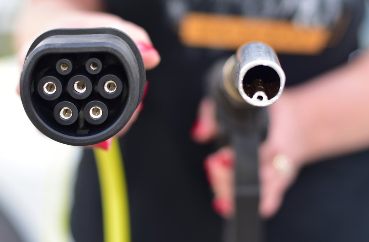 Nahaufnahme von zwei verschiedenen Ladesteckern für Elektrofahrzeuge, einer mit sieben runden Kontakten und einer mit einem runden Hohlstecker.